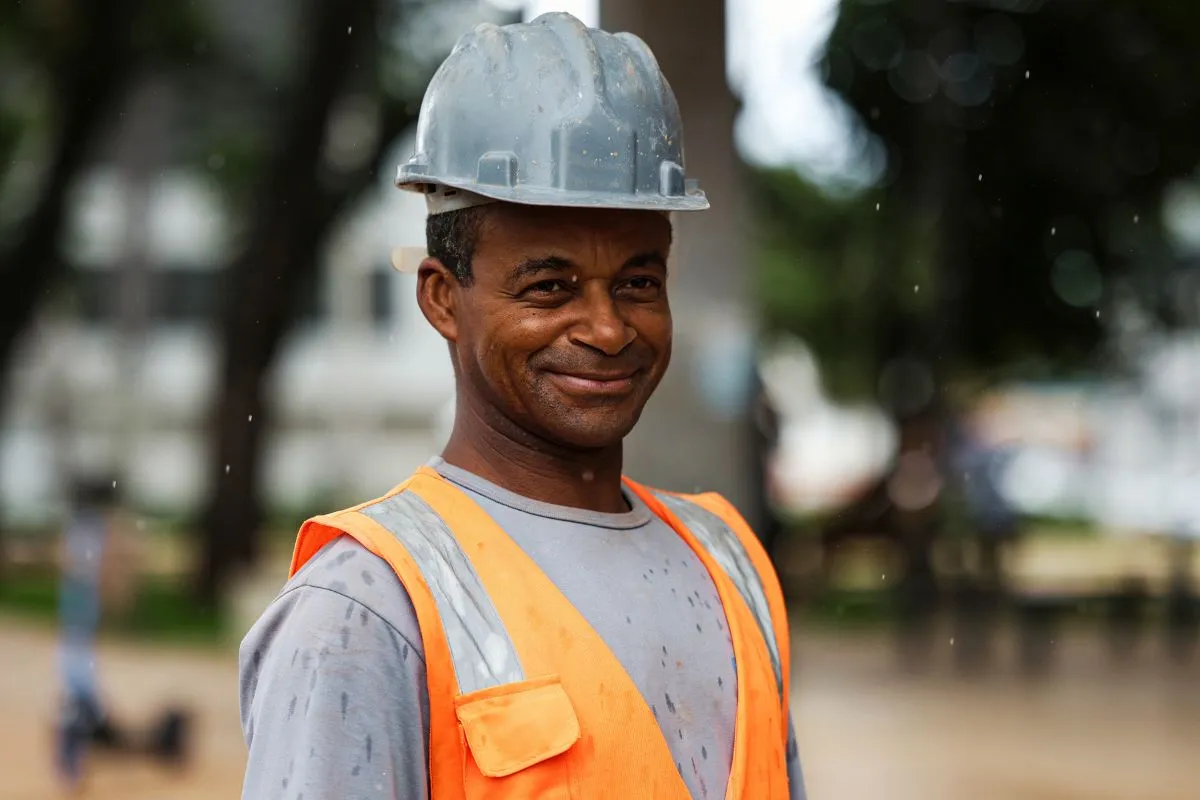 Trabalhador usando capacete e colete de segurança em ambiente urbano durante atividade profissional.