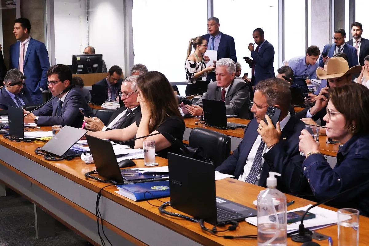 Autoridades reunidas em sessão de inquérito institucional, utilizando computadores e celulares durante reunião