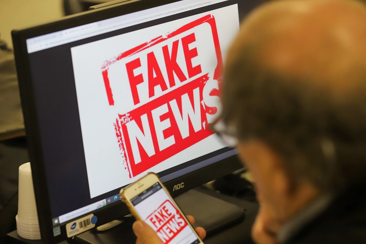 Imagem mostra alerta de fake news em tela de computador e celular, destacando desinformação em conteúdos digitais.