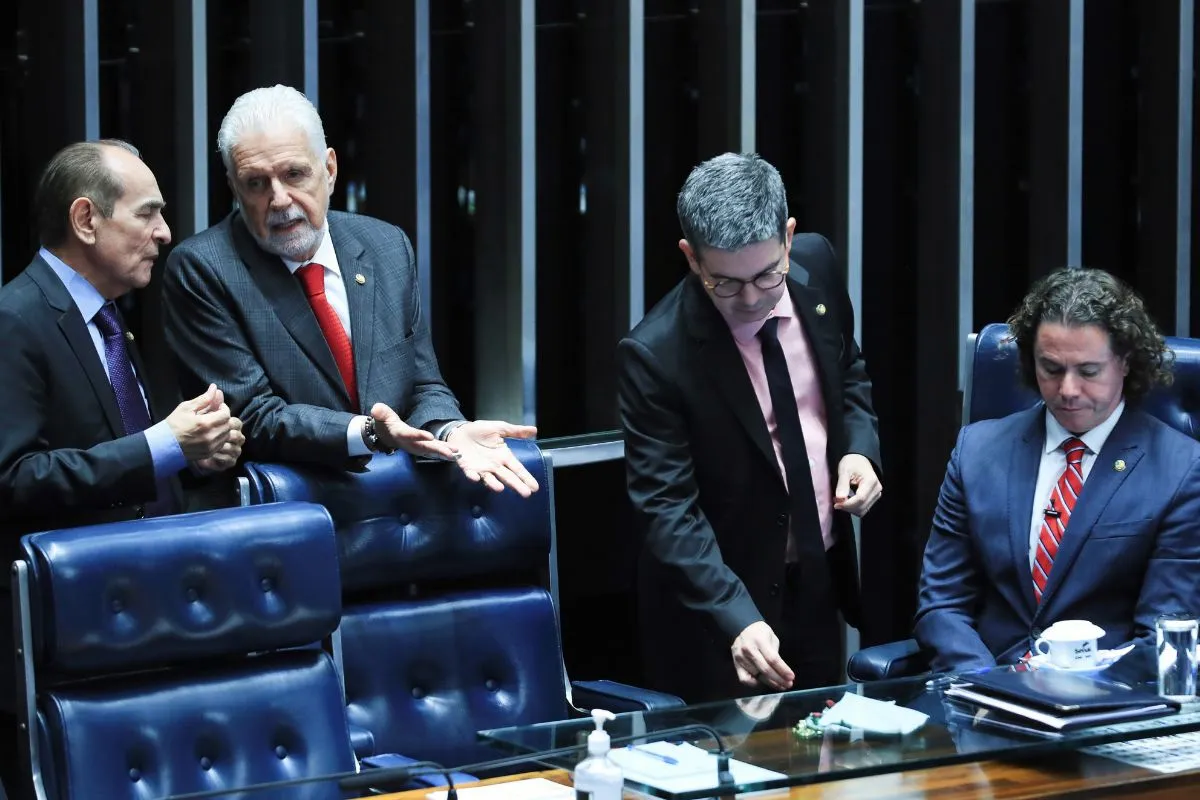 Parlamentares conversam durante sessão no plenário do Senado Federal, em ambiente formal com cadeiras azuis e mesa de votação.