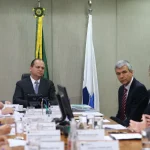 Autoridades reunidas em mesa de reunião institucional discutindo temas administrativos