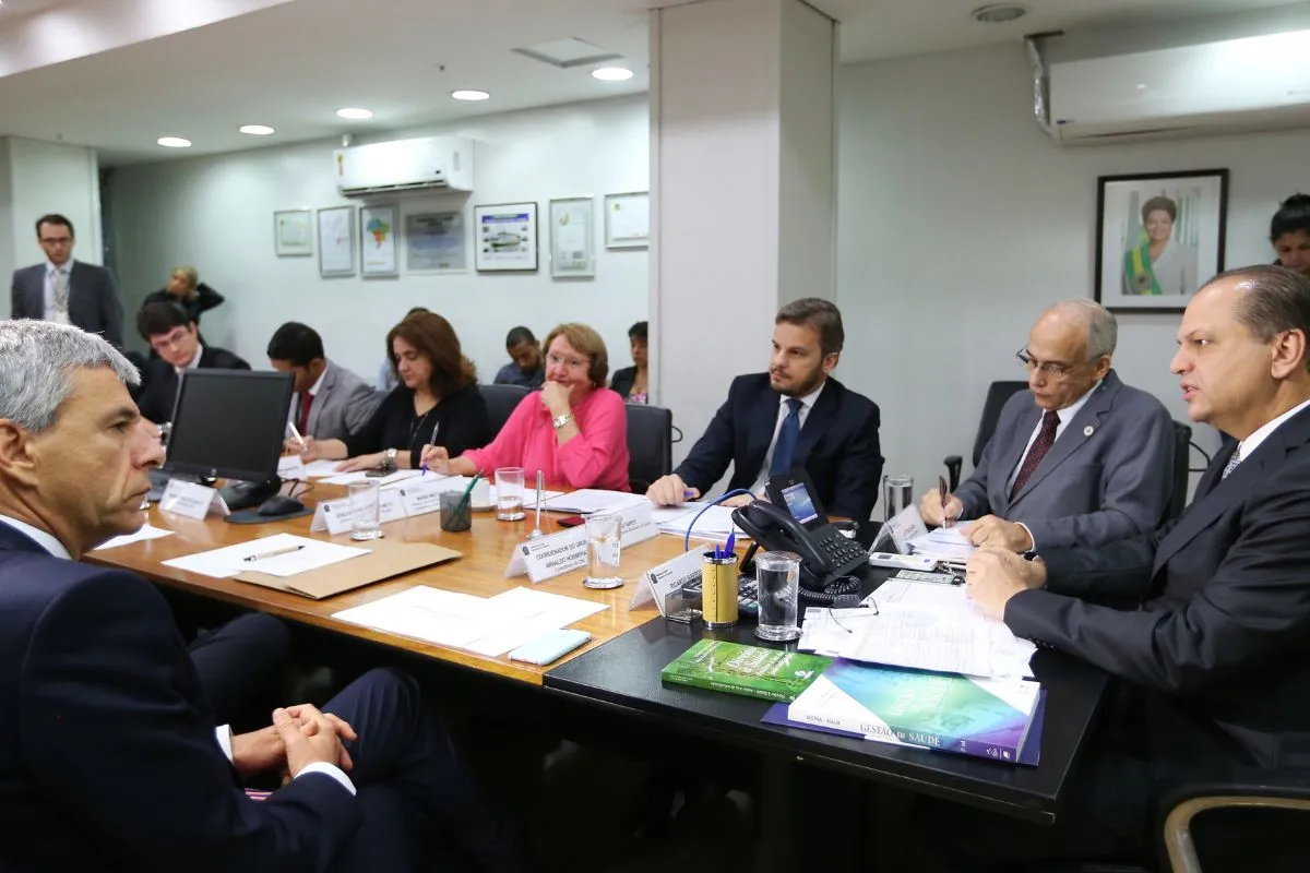 Autoridades reunidas em mesa de reunião institucional discutindo temas administrativos