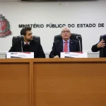 Autoridades do Ministério Público sentadas à mesa durante coletiva oficial em sala institucional.