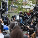 Jornalistas seguram microfones e celulares durante entrevista em cobertura de notícia política ao ar livre.
