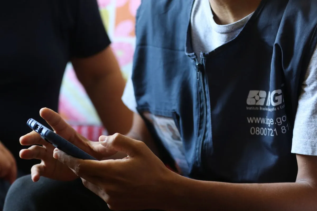 Agente do IBGE usando celular para coleta de dados durante pesquisa domiciliar do Censo.