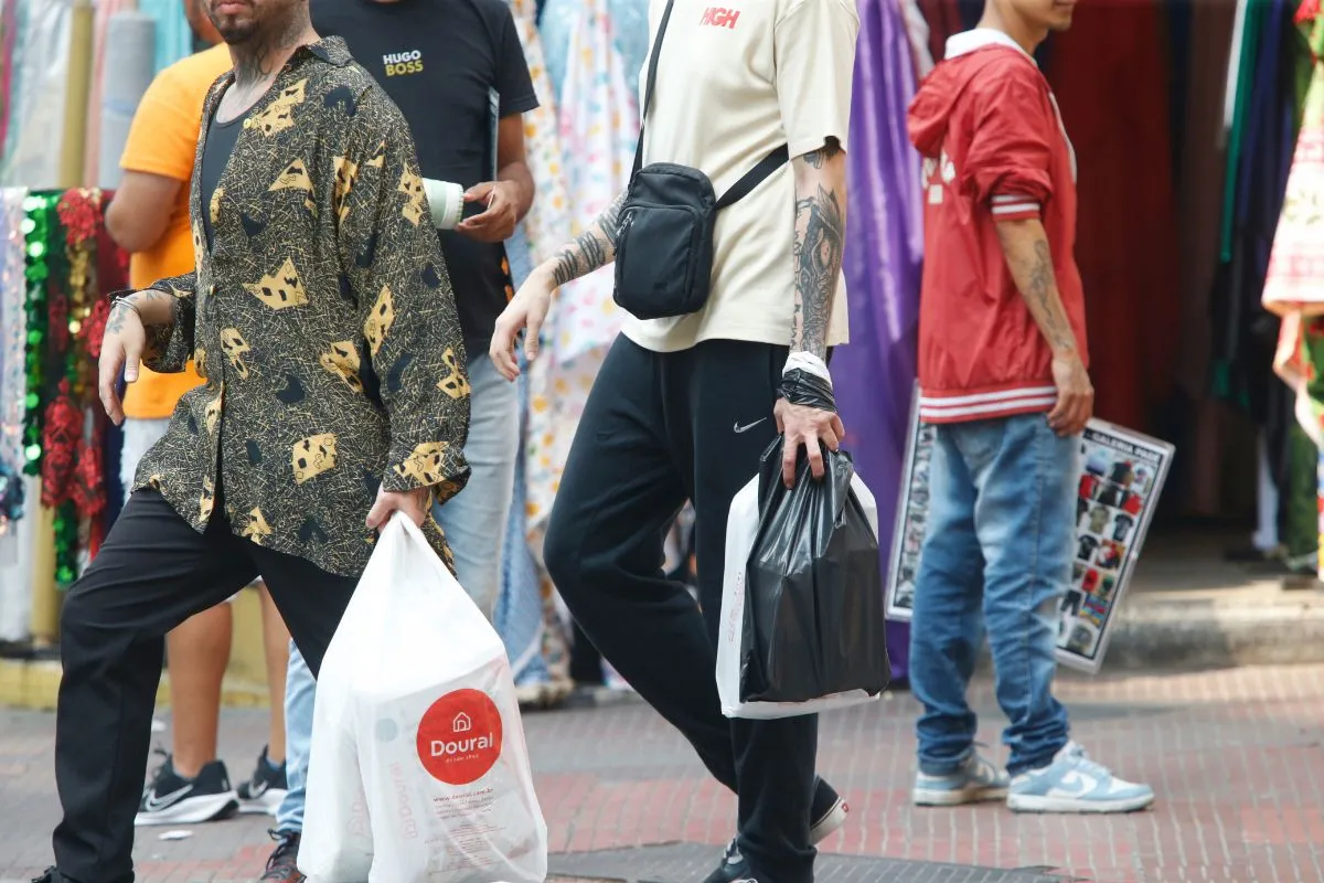 Pessoas caminhando com sacolas de compras em área comercial de rua