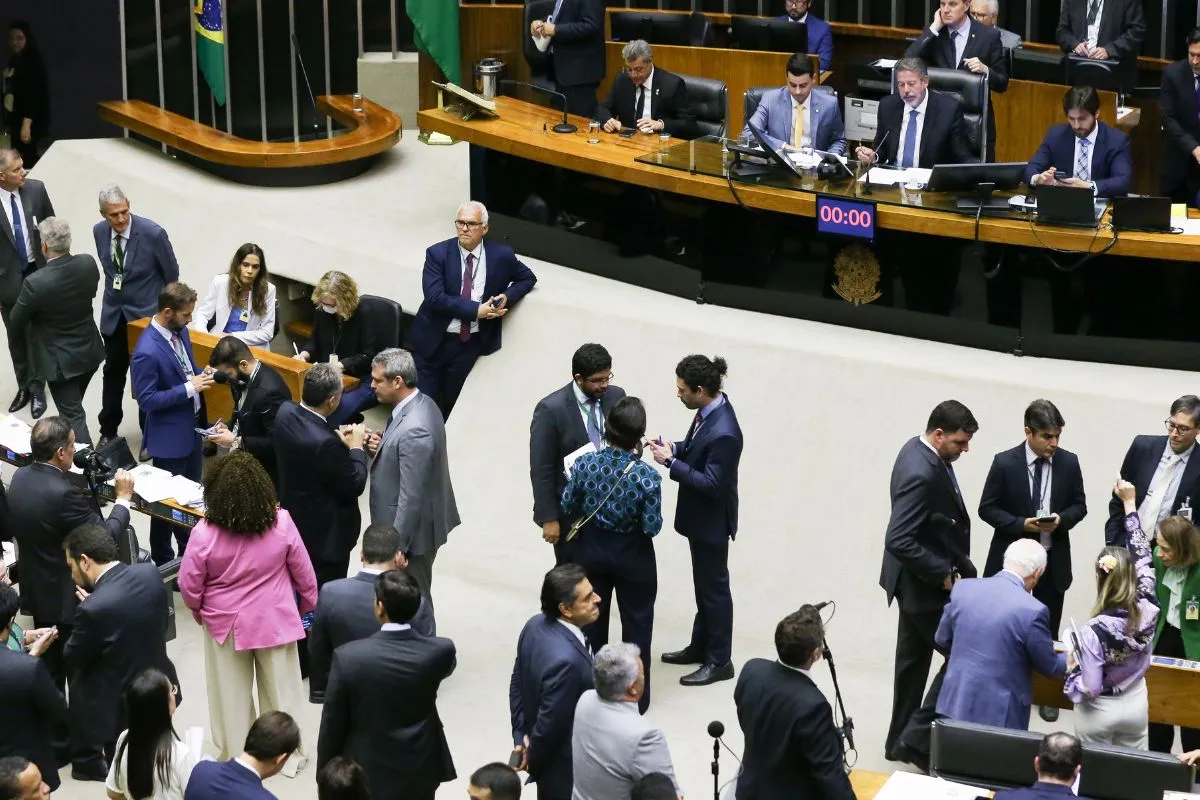 Parlamentares reunidos no plenário da Câmara dos Deputados durante sessão legislativa, com grupos conversando e mesa diretora ao fundo.