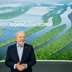 Presidente Lula em evento da COP30 Amazônia com imagem aérea da floresta amazônica ao fundo.