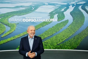 Presidente Lula em evento da COP30 Amazônia com imagem aérea da floresta amazônica ao fundo.