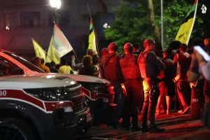 Policiais acompanham manifestação noturna com bandeiras e viatura ao fundo no Brasil violência