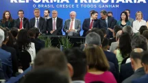 Autoridades políticas participam de evento institucional sobre reforma tributária, com público e painel oficial ao fundo.