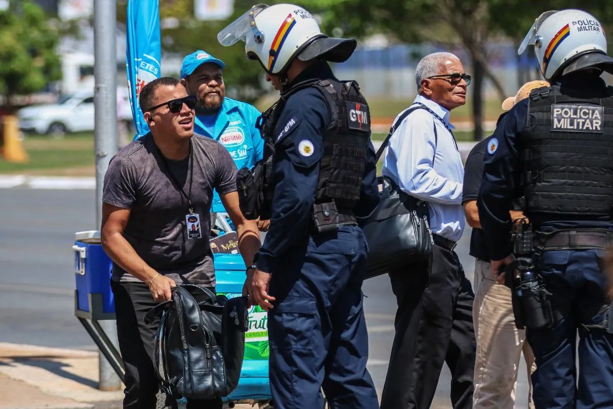 Policiais militares abordam homem com mochila em via pública durante ação de segurança em cidade brasileira.