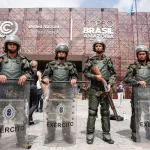 Militares do Exército Brasileiro com escudos de proteção em frente ao prédio da COP30 Brasil em Belém, durante evento da ONU sobre mudanças climáticas.