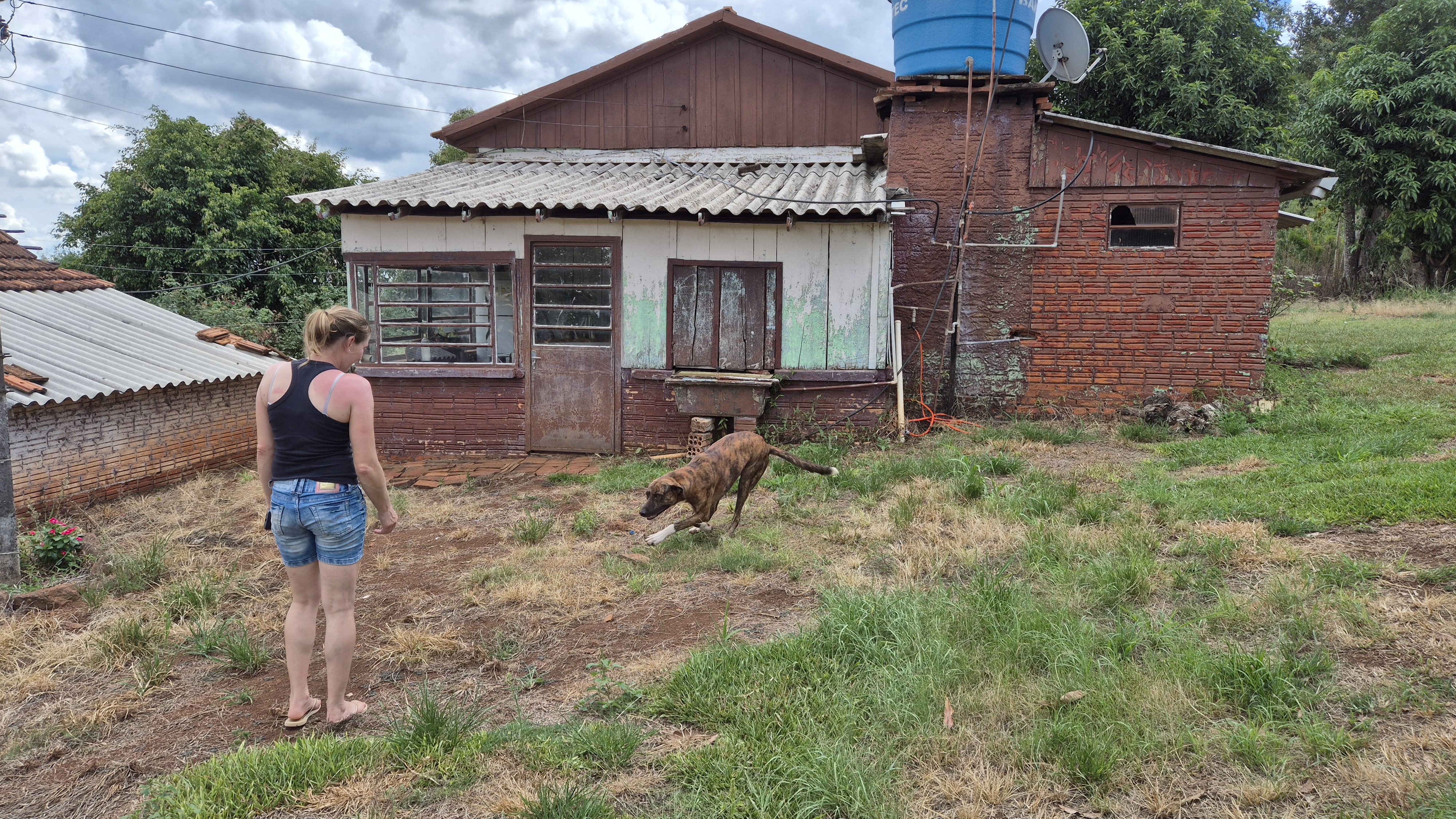 Patrícia Eberhard, irmã de Fernando, em frente a sua antiga casa na fazenda repartida com o irmão. A atual moradora de Humaitá brinca com o cachorro Bilu | Foto: Tauany Cattan/Revista Oeste