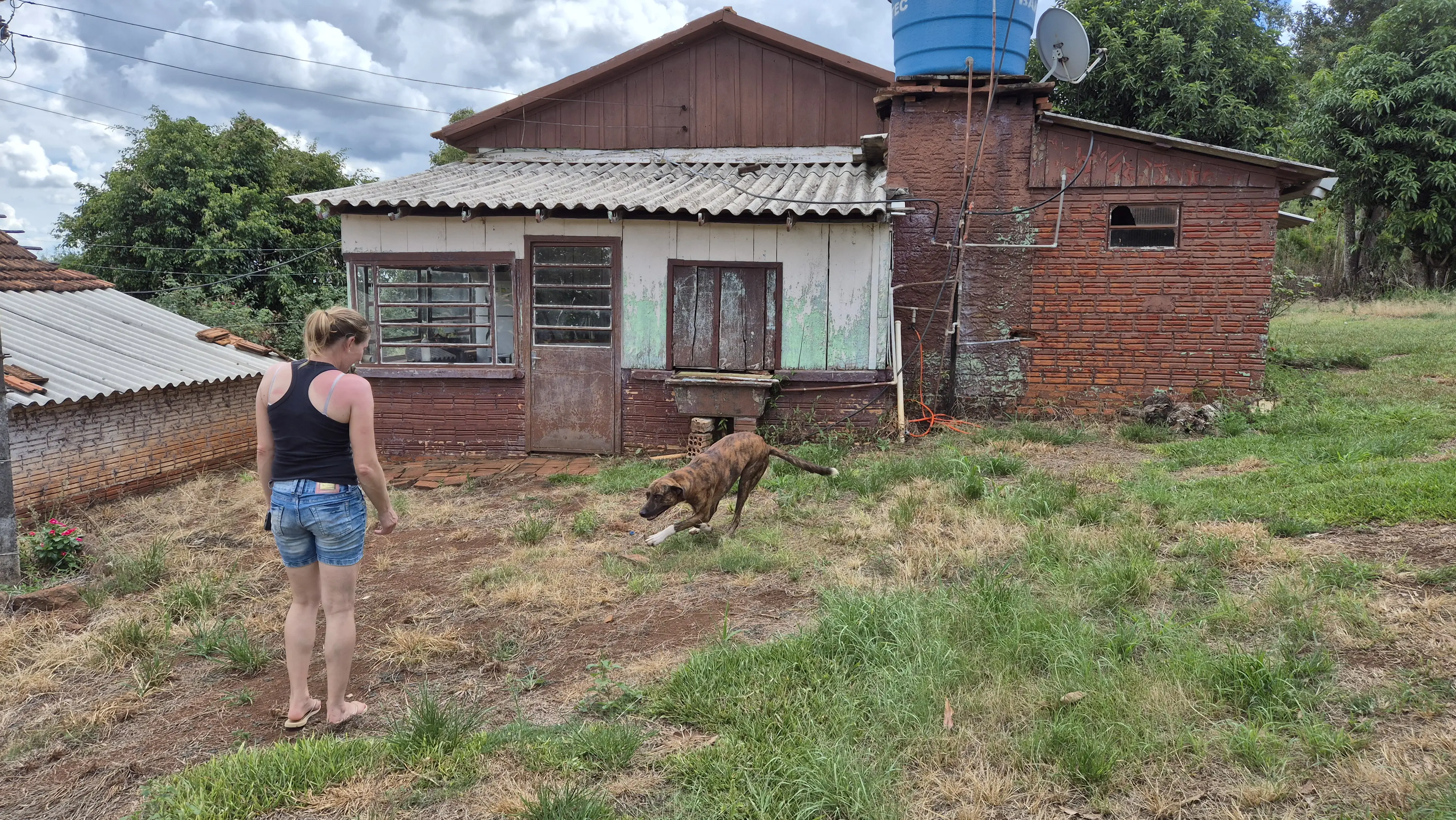 Patrícia Eberhard, irmã de Fernando, em frente a sua antiga casa na fazenda repartida com o irmão. A atual moradora de Humaitá brinca com o cachorro Bilu | Foto: Tauany Cattan/Revista Oeste