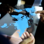 Mãos apontando para mapa mundial digital em tela transparente representando análise geopolítica global