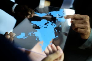 Mãos apontando para mapa mundial digital em tela transparente representando análise geopolítica global