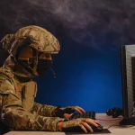 Soldado com equipamento tático utilizando computador em operação de guerra cibernética