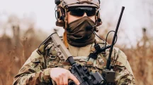 Soldado com uniforme camuflado e arma em posição de prontidão durante operação militar