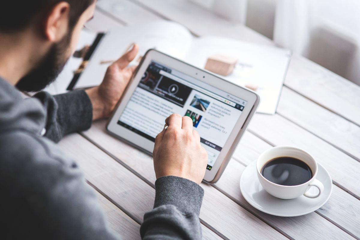 Homem lendo notícias em um tablet enquanto toma café em uma mesa