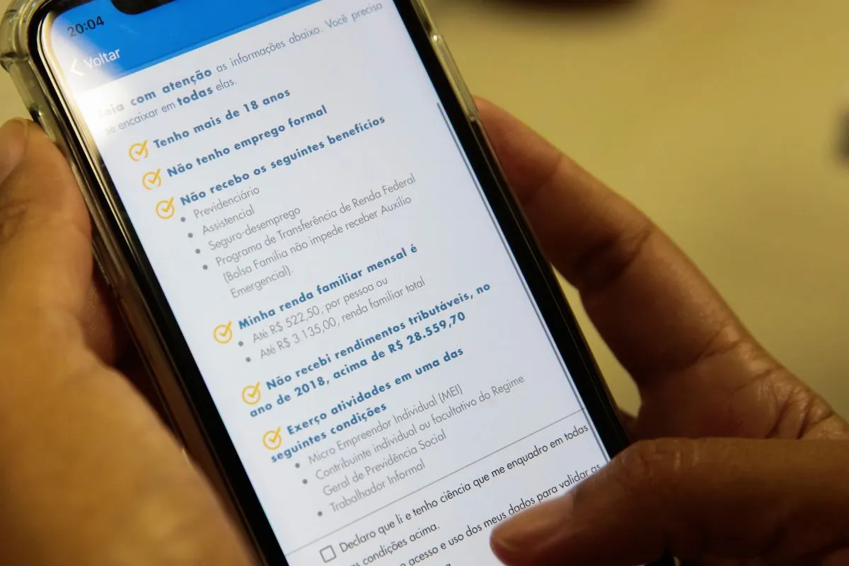 Pessoa verificando requisitos para receber Auxílio Emergencial em aplicativo do governo no celular