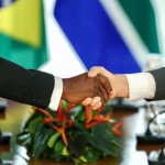 Aperto de mãos entre representantes internacionais com bandeiras ao fundo simbolizando acordo diplomático