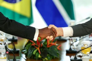 Aperto de mãos entre representantes internacionais com bandeiras ao fundo simbolizando acordo diplomático