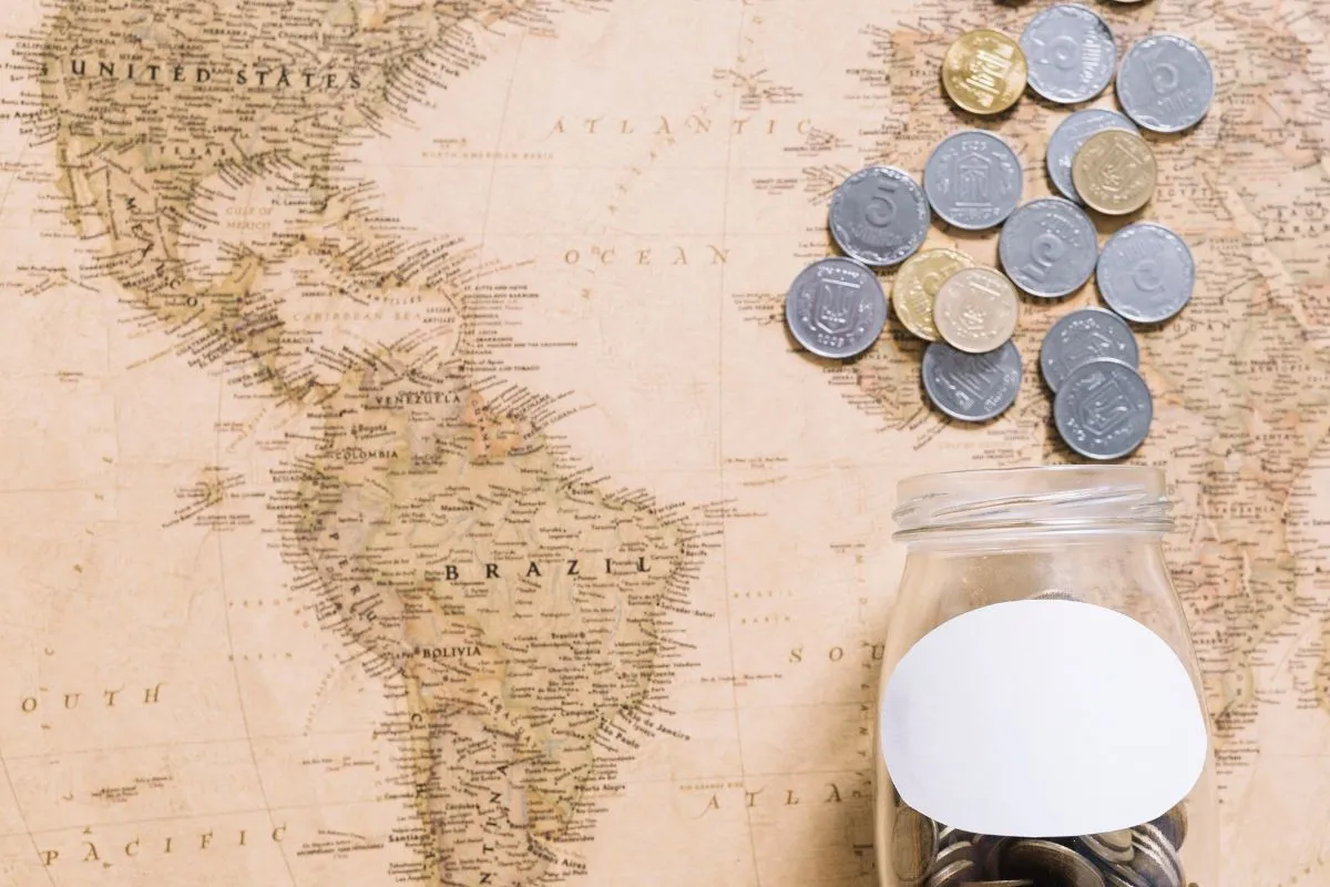 Moedas caindo em um pote sobre mapa-múndi antigo representando economia global e finanças internacionais