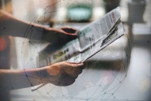 Pessoa segurando e lendo um jornal impresso com sobreposição de gráfico digital representando rede global de notícias e informação