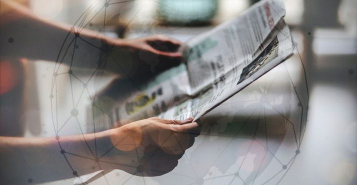 Pessoa segurando e lendo um jornal impresso com sobreposição de gráfico digital representando rede global de notícias e informação