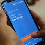 Pessoa utilizando aplicativo do Auxílio Emergencial no celular para consultar benefício social