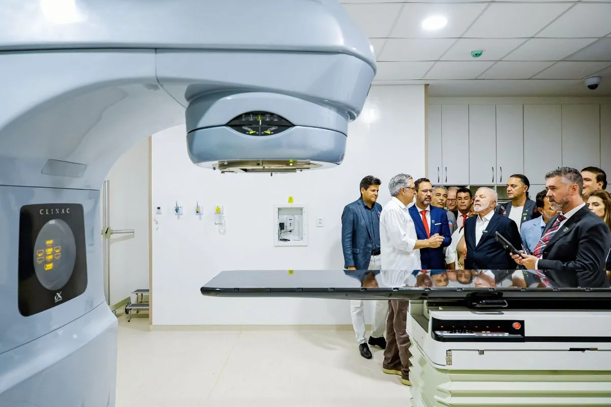 Autoridades e médicos observam equipamento de radioterapia em hospital durante visita institucional