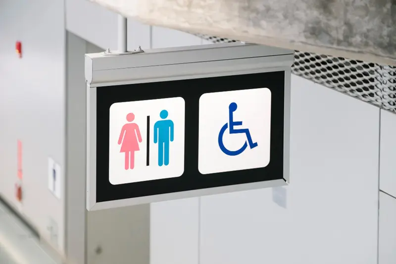 Placa mostra opções de banheiros masculino, feminino e para pessoas com deficiência, em alusão à nota sobre proibição de uso de banheiro feminino por trans em Campo Grande