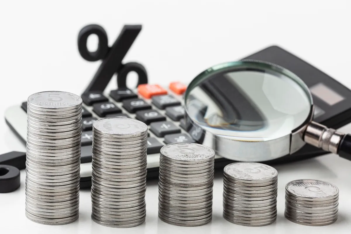 Pilhas de moedas ao lado de calculadora, lupa e símbolo de porcentagem representando análise financeira e juros