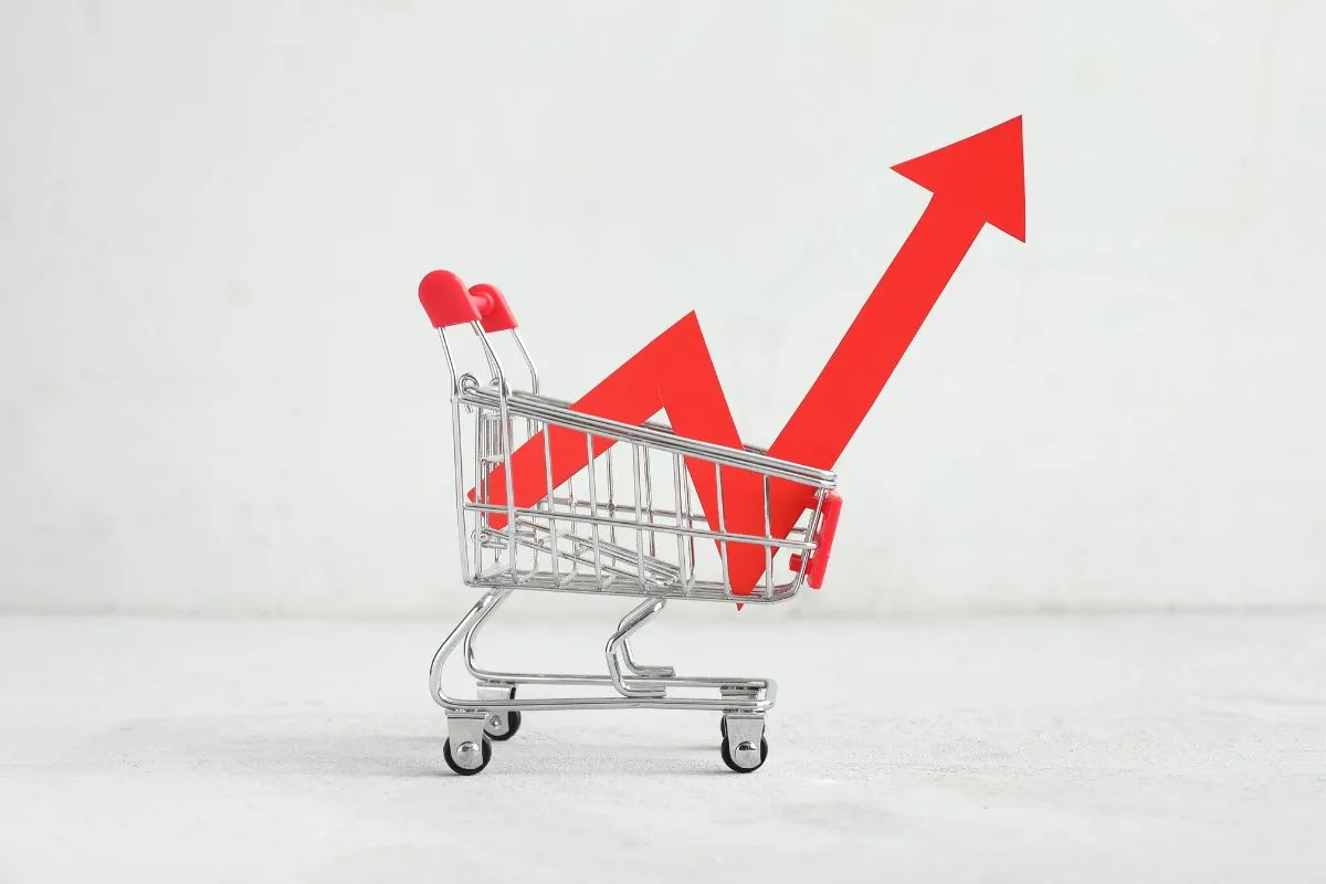 Carrinho de supermercado com seta vermelha ascendente representando inflação e aumento de preços