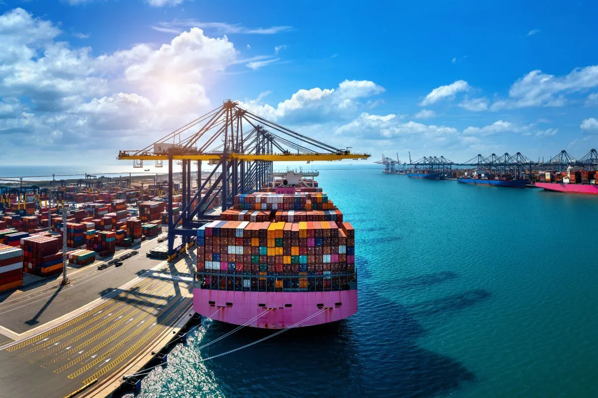 Navio de contêineres sendo carregado em porto com guindastes, representando logística e comércio internacional