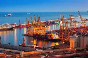 Porto com guindastes, navios cargueiros e contêineres representando comércio internacional e transporte marítimo