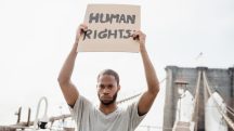 Homem segurando cartaz escrito “Human Rights” em manifestação por direitos humanos