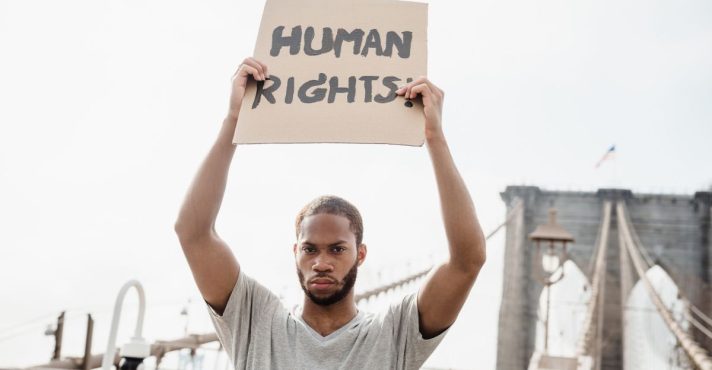 Homem segurando cartaz escrito “Human Rights” em manifestação por direitos humanos