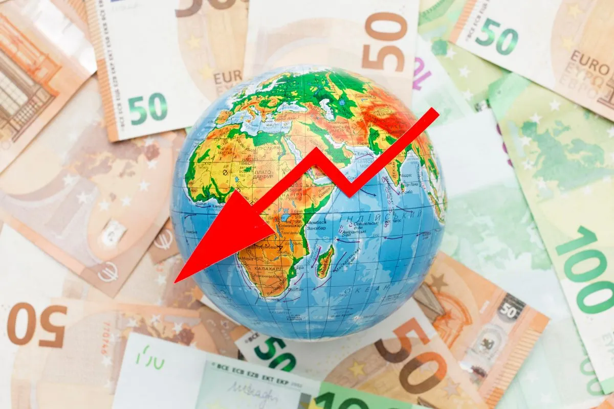 Globo terrestre sobre notas de euro com seta vermelha apontando para baixo representando crise econômica global
