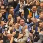 No centro da imagem, de terno claro, Flávio comemora resultado no Senado em meio a dezenas de aliados | Foto: Reprodução/X/@FlavioBolsonaro