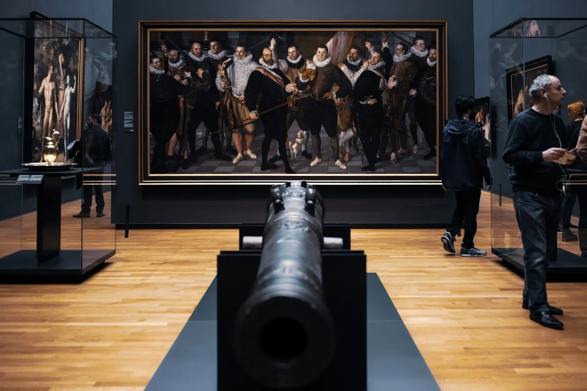 Interior de museu com pintura histórica de soldados e canhão antigo em primeiro plano