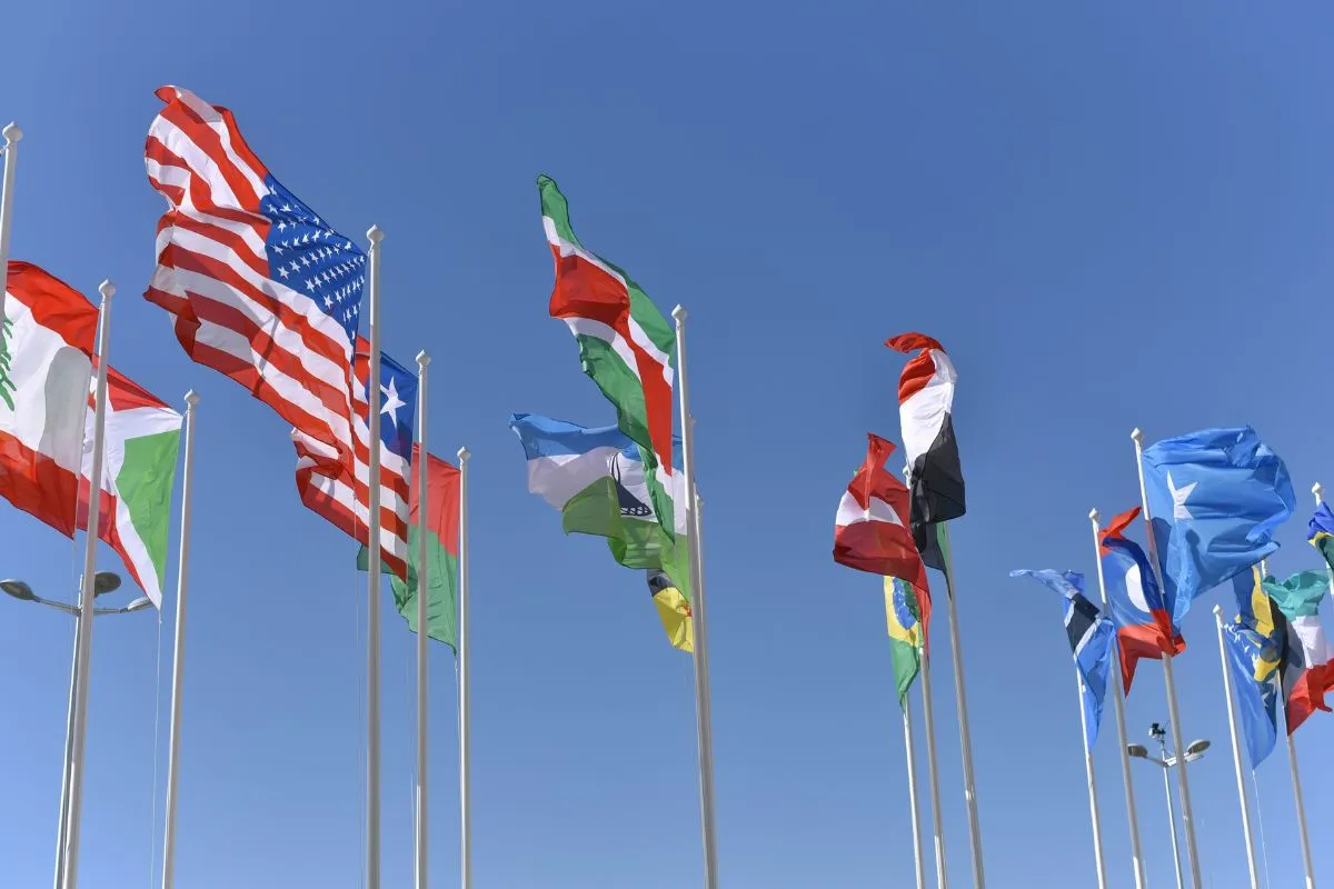 Bandeiras de diversos países, incluindo Estados Unidos e nações internacionais, tremulando em mastros sob céu azul