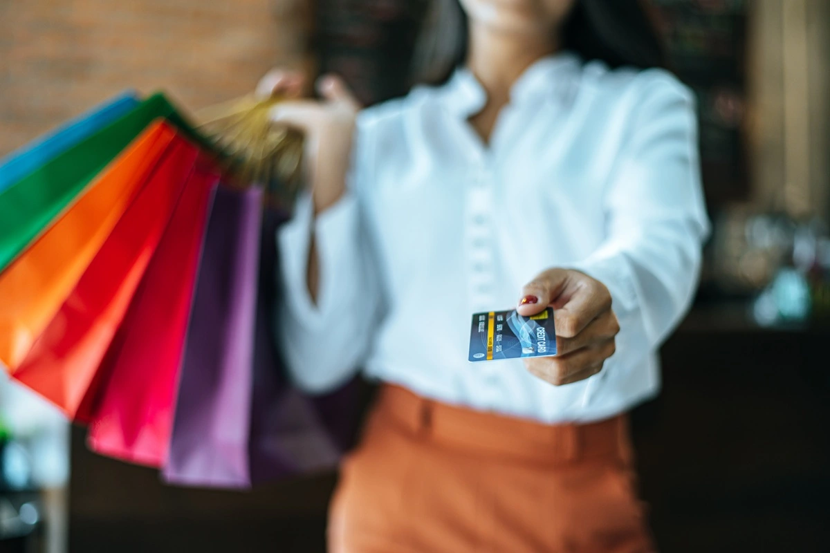 Mulher segurando cartão de crédito e sacolas de compras representando consumo e poder de compra