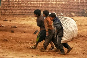 Crianças carregando saco pesado em área pobre representando trabalho infantil e desigualdade