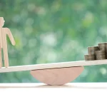 Balança com figura de pessoa de um lado e moedas do outro representando desigualdade econômica e poder de compra