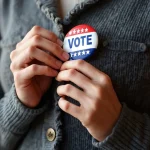 Pessoa prendendo botão com palavra vote simbolizando participação eleitoral