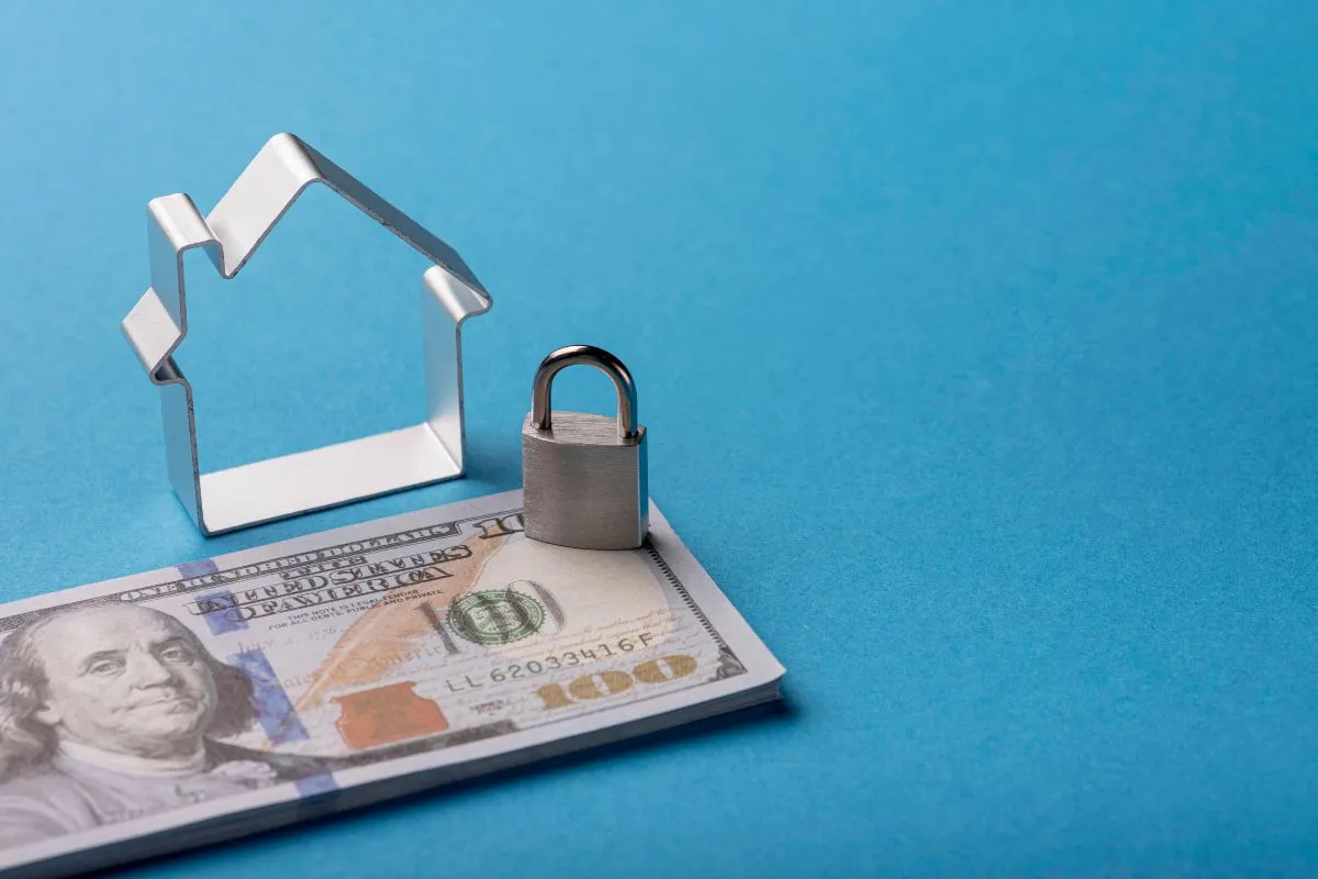 Cadeado sobre nota de dólar ao lado de ícone de casa representando segurança financeira e proteção de patrimônio