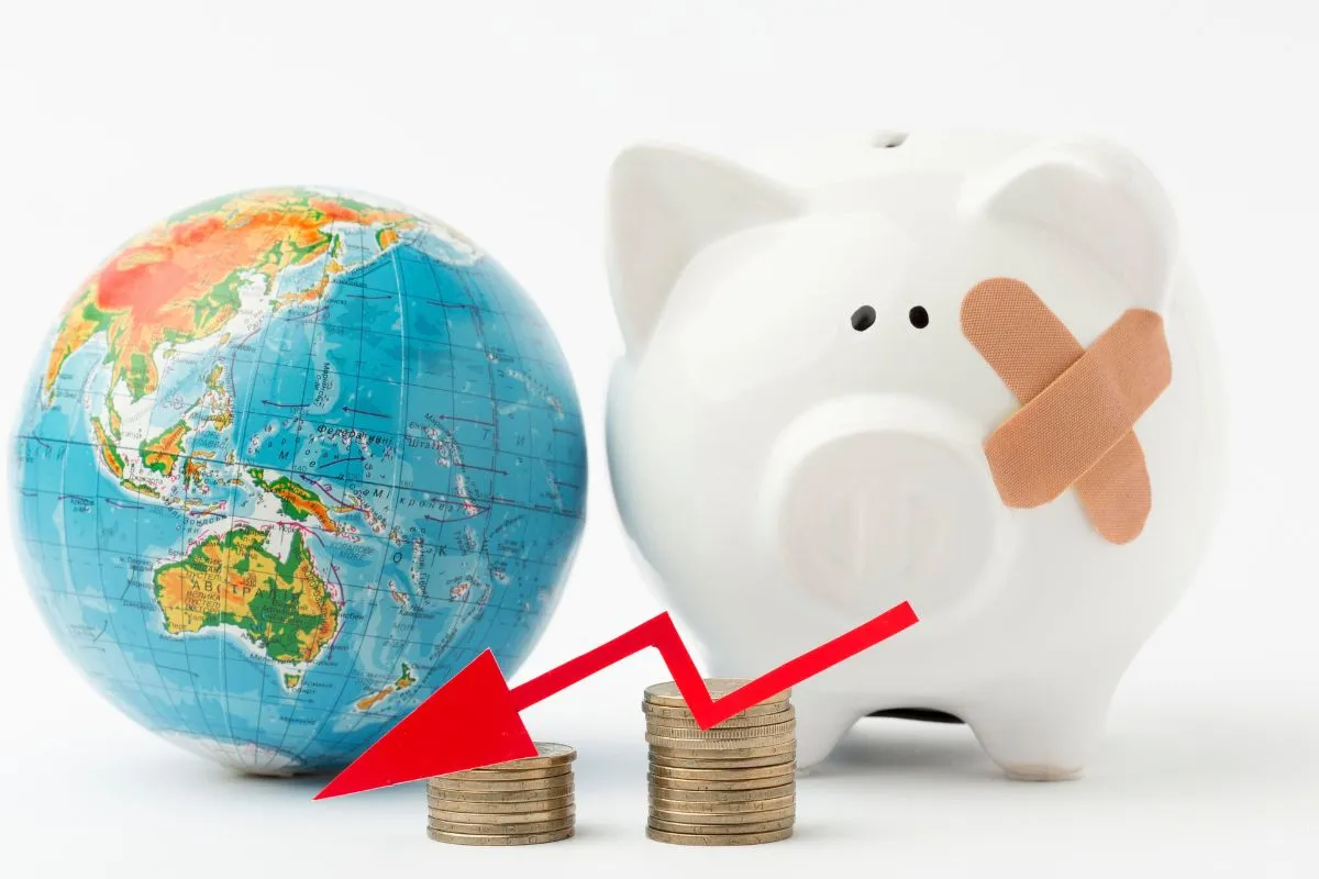 Globo terrestre ao lado de cofrinho com curativo e moedas com seta de queda representando crise econômica