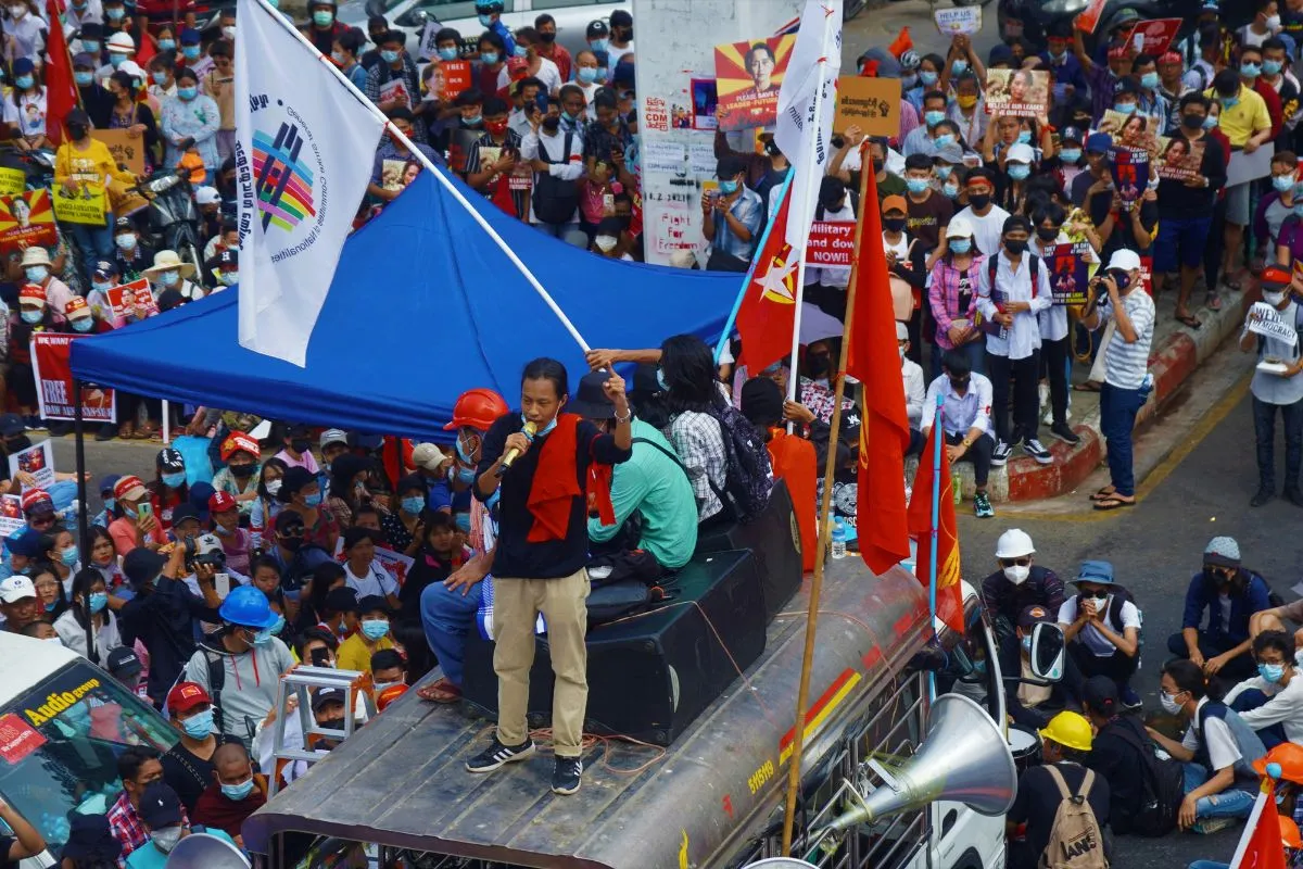 Multidão em protesto com ativista discursando em cima de veículo usando megafone